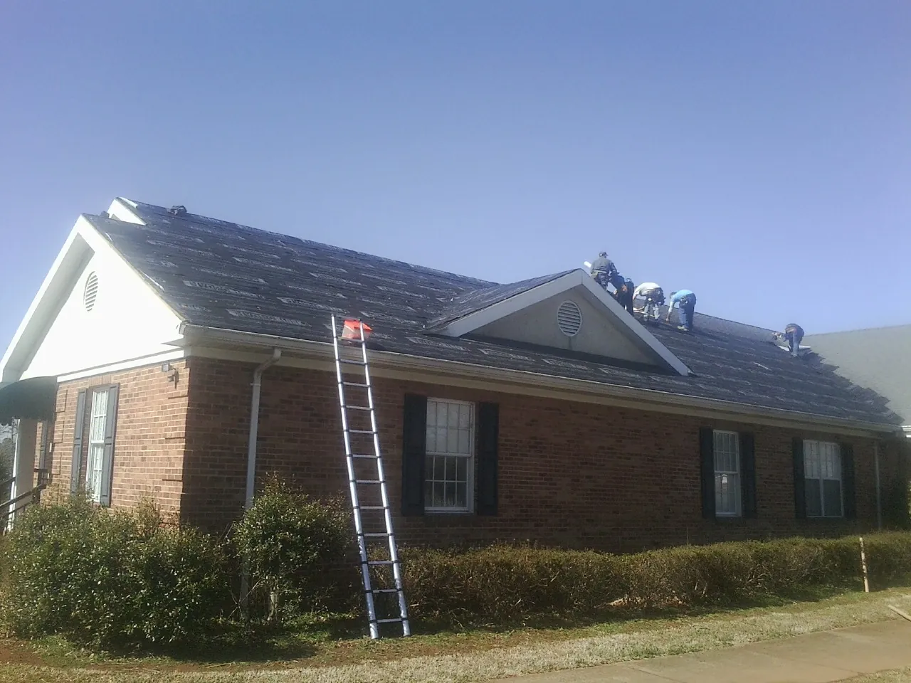 Crew tearing shingles off a brick ranch roof with a ladder set — Emergency Roof Repair work by our crew in Poquoson