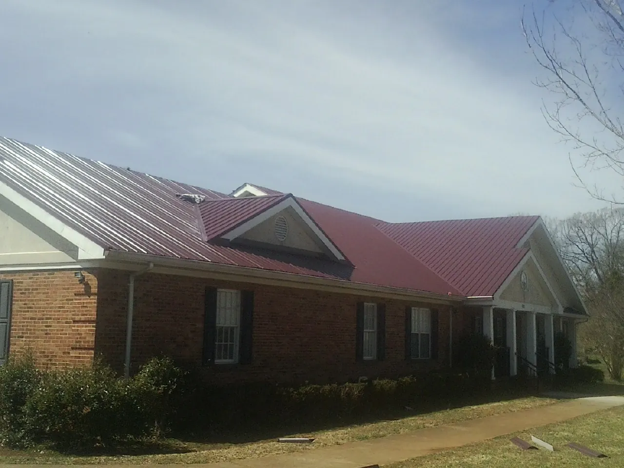 Red metal roof with gabled entries on a long brick building, from a Hail Damage Roof Repair job in Poquoson