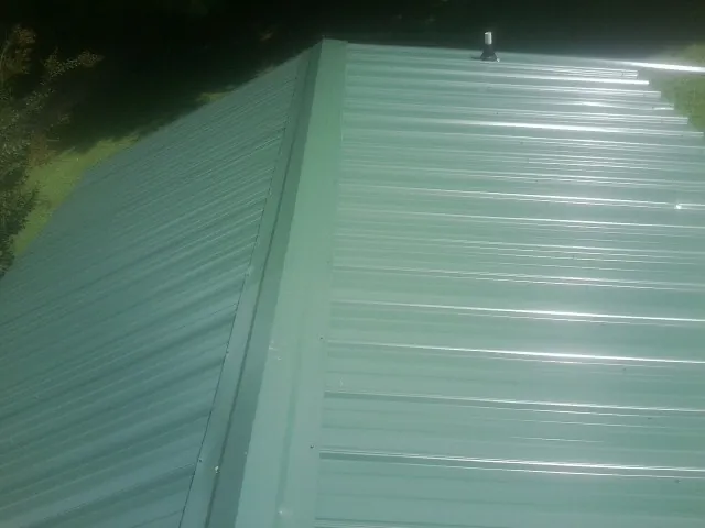 New green metal panels meeting at the ridge of a roof — Flat Roof Repair work by our crew in Poquoson