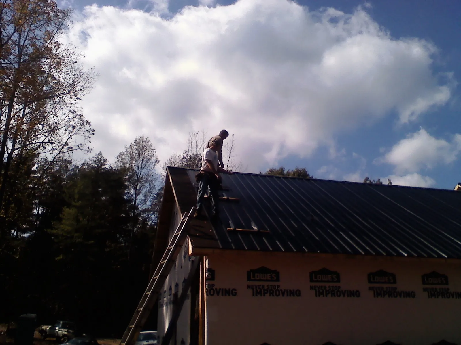 Roofer fastening dark metal panels high against a cloudy sky, from a Roof Inspection job in Poquoson