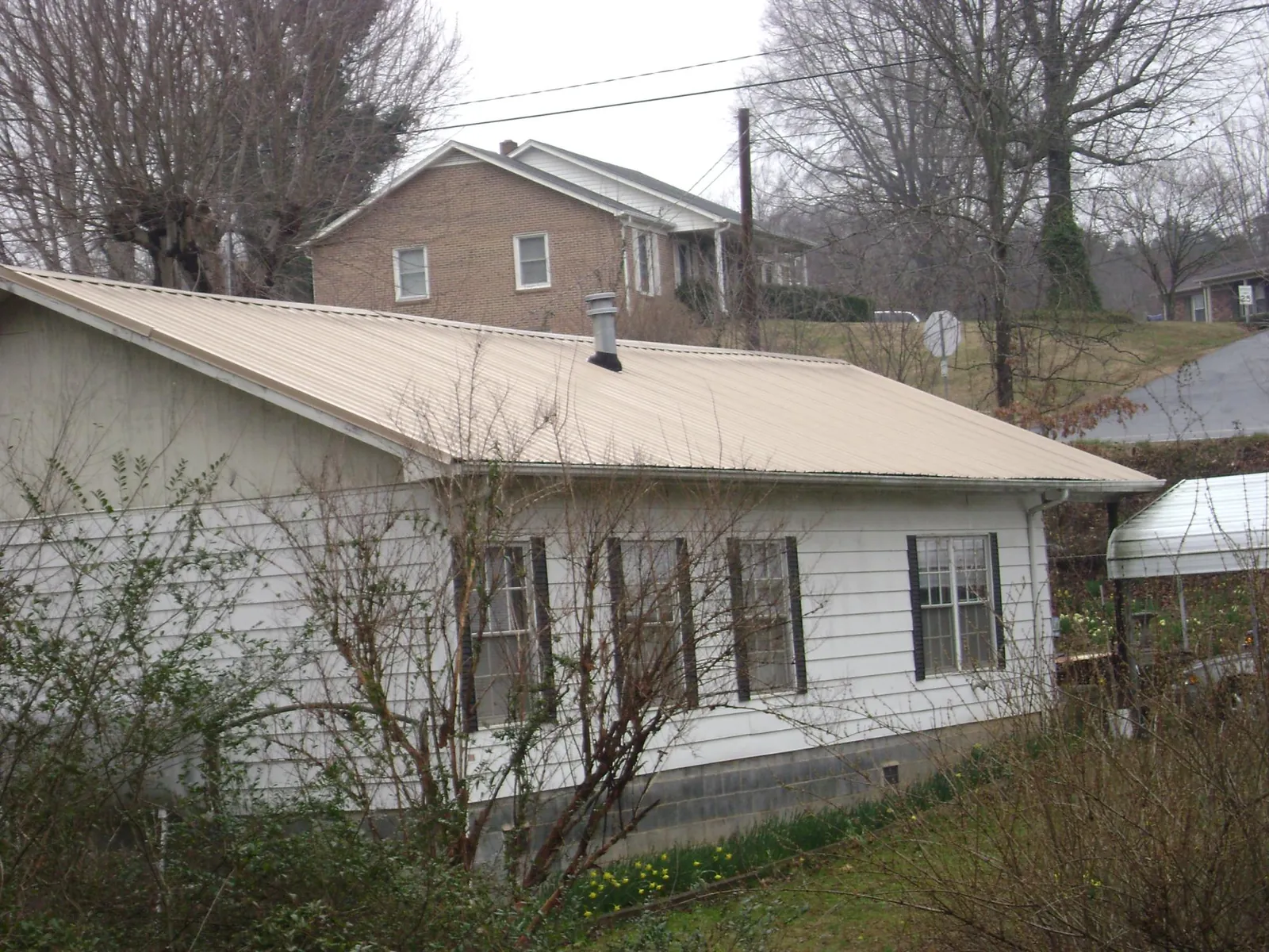 Tan metal roof on a white sided house set into a hillside — Commercial Roofing by Roofing Brothers in Poquoson